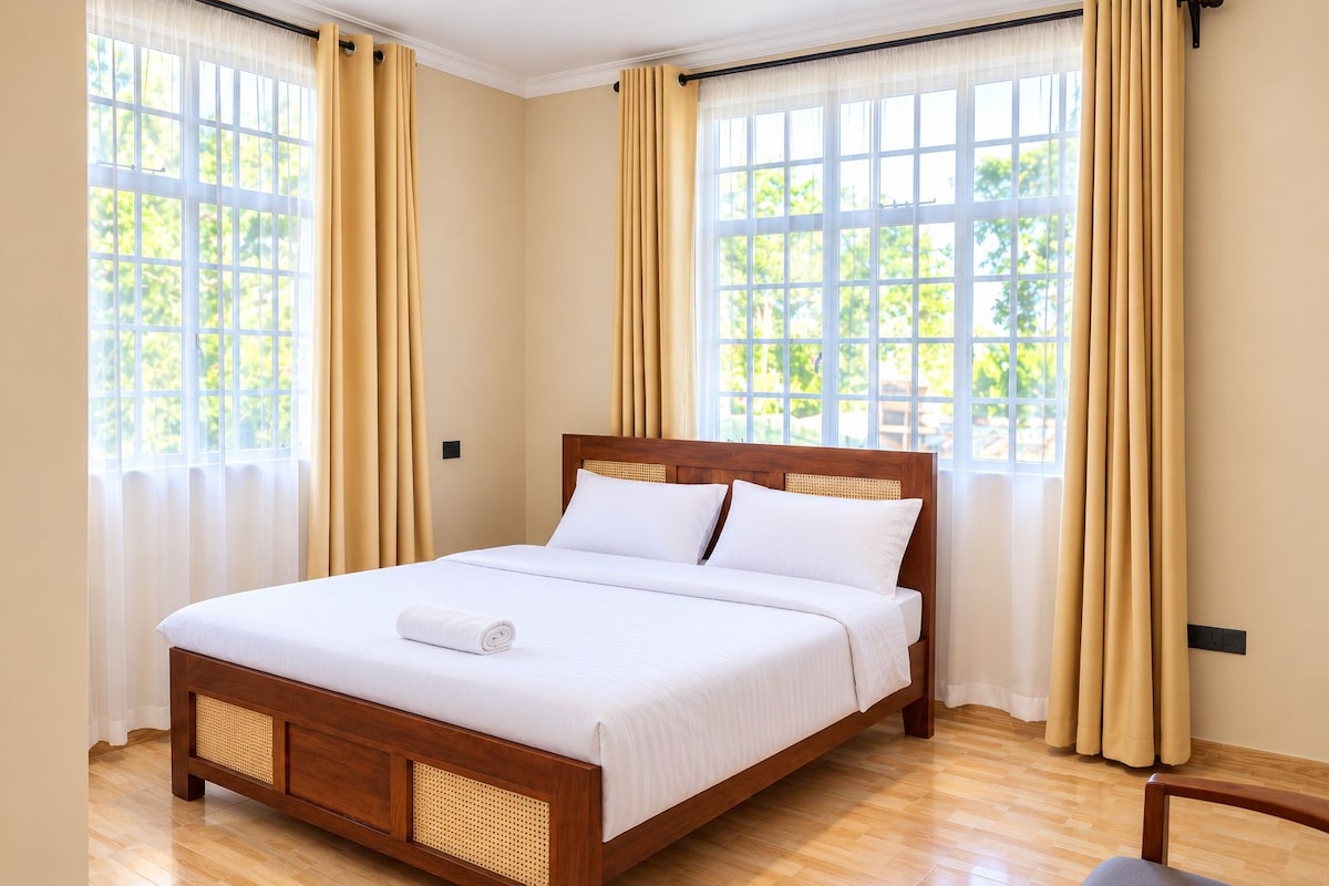 A hotel room with a wooden bed, beige curtains, and large windows.
