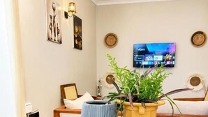 A wooden dining table with two potted plants, a television mounted on the wall, and a framed picture on the wall. - The Valley Retreat (Arusha)