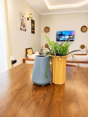 Una mesa de comedor de madera con dos plantas en macetas, un televisor montado en la pared y un cuadro enmarcado.
