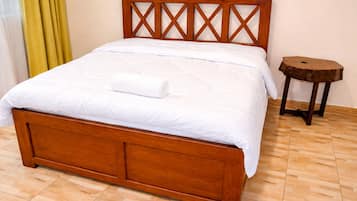A wooden bed with a cross-back design, a white bedspread, and a small round wooden stool beside it.