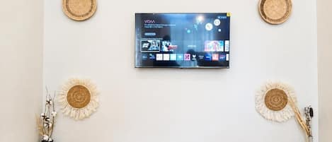 Ein Flachbildfernseher an einer weißen Wand, begleitet von zwei gewobenen Wanddekorationen.