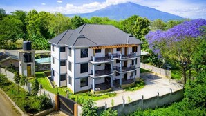 A multi-story building with a flat roof, surrounded by greenery and a mountain in the background. - The Valley Retreat (Arusha)