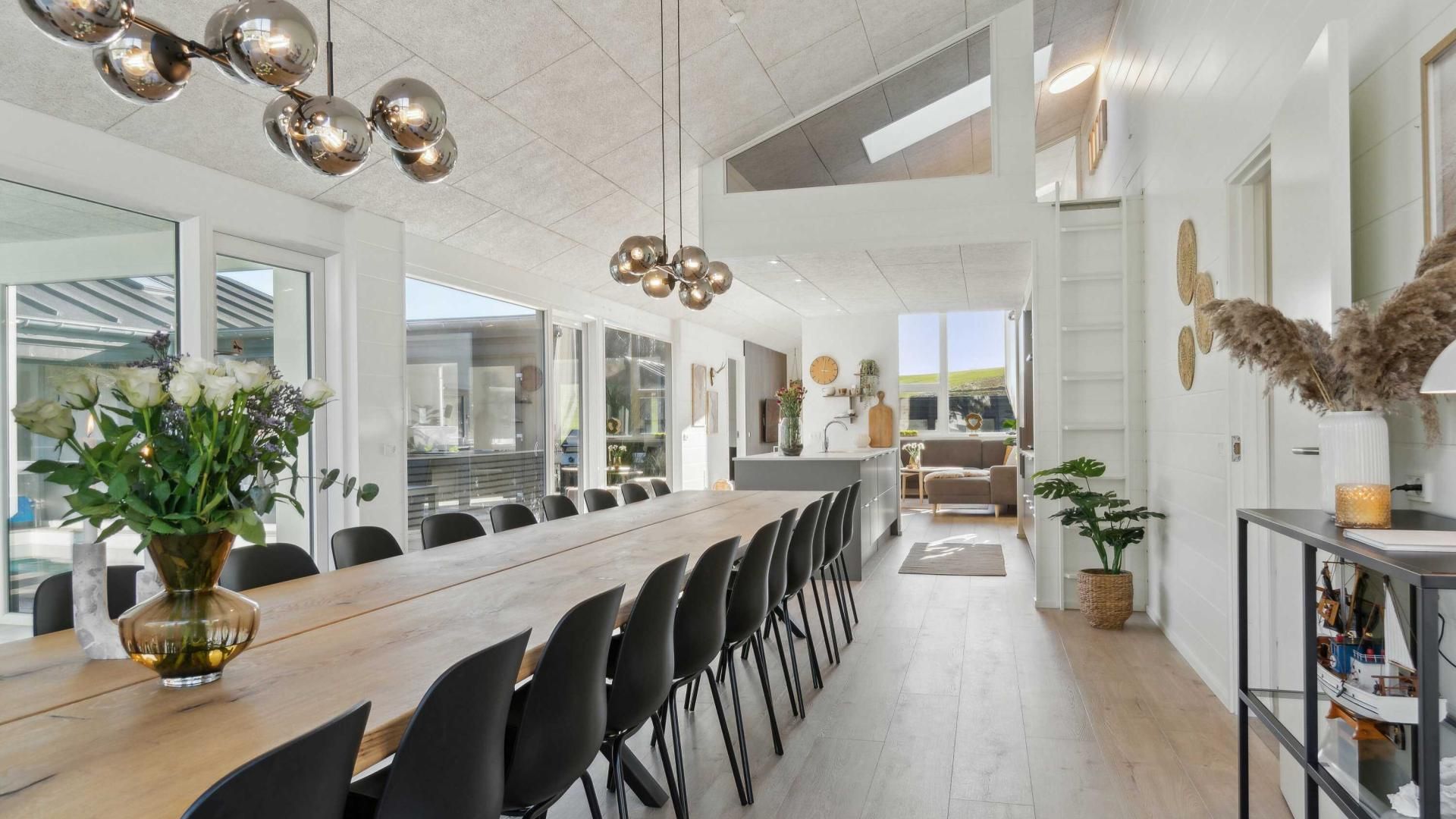 Un'elegante sala da pranzo con un lungo tavolo in legno, sedie nere e un vaso decorativo con fiori.