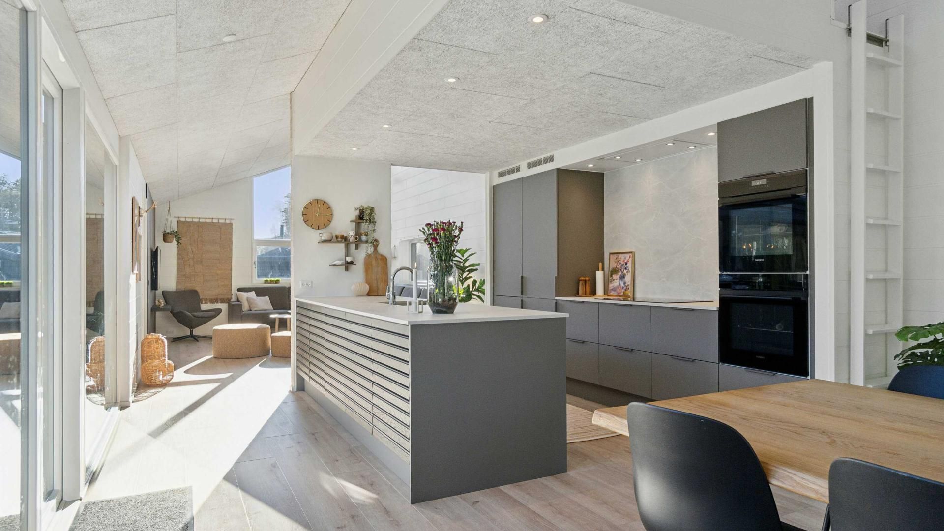 A modern kitchen with a central island, a dining area with a wooden table, and a living space with a sofa and chairs.