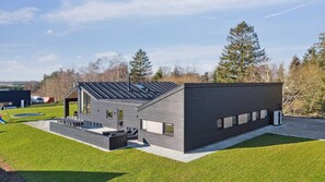 Ein modernes Haus mit Flachdach, einer Terrasse und Gartenmöbeln sowie einem gepflegten Rasen.