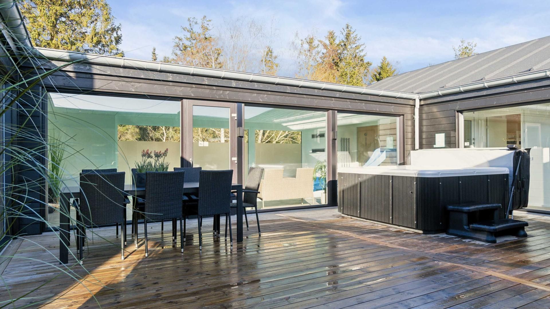 Eine moderne Terrasse im Freien mit Whirlpool, Glasüren und Gartenmöbeln.