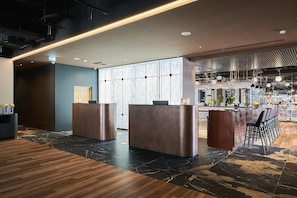 Uma área de recepção moderna com piso de mármore, dois balcões de atendimento e um espaço de bar com assentos.