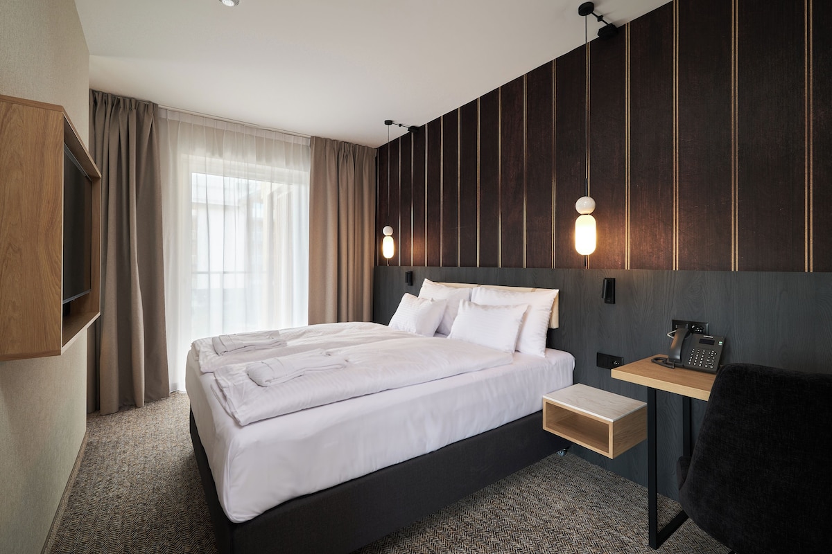 A hotel room with a large bed, bedside table, and a desk with a phone.