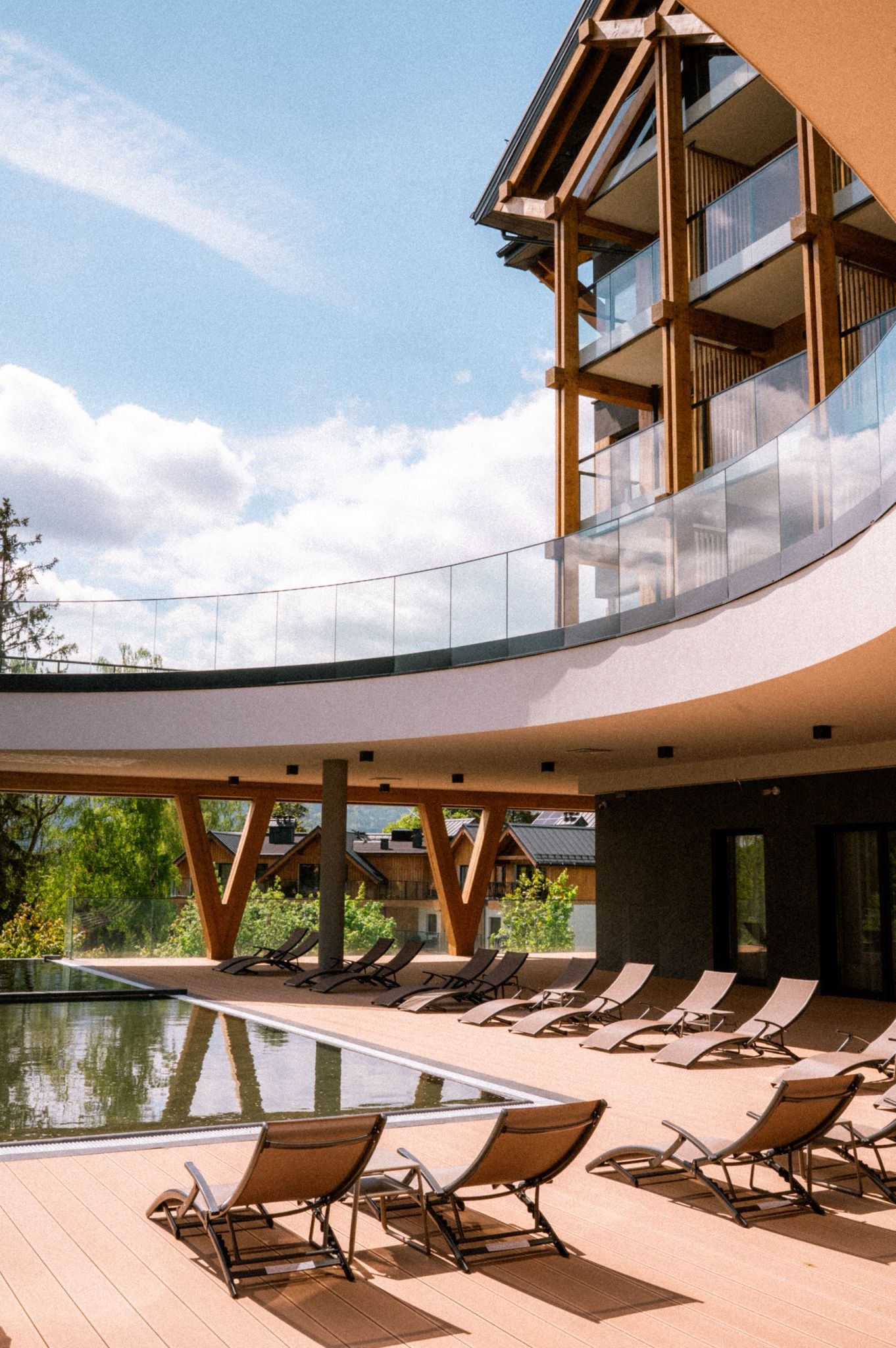 A modern building with a pool area, sun loungers, and a glass balustrade.