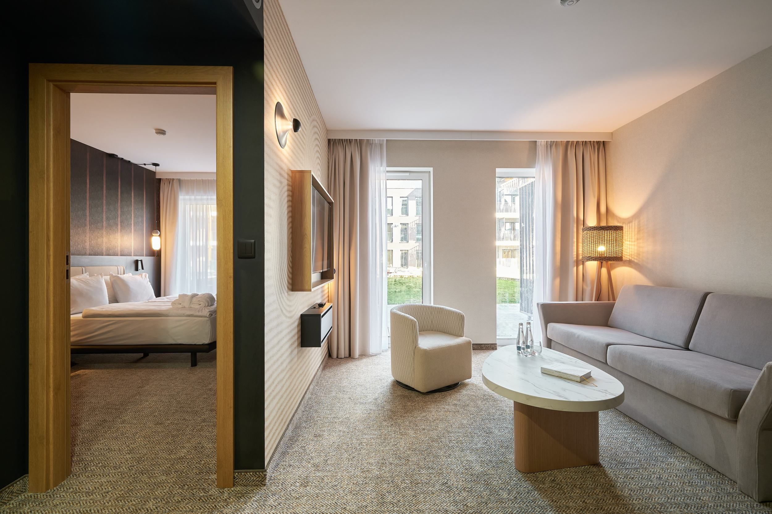 A hotel room with a bed, a sofa, a chair, a coffee table, and a TV mounted on the wall.
