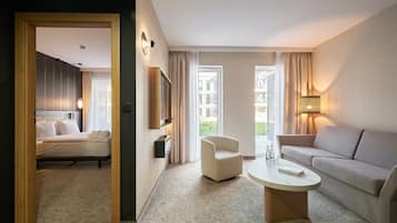 A hotel room with a bed, a sofa, a chair, a coffee table, and a TV mounted on the wall.