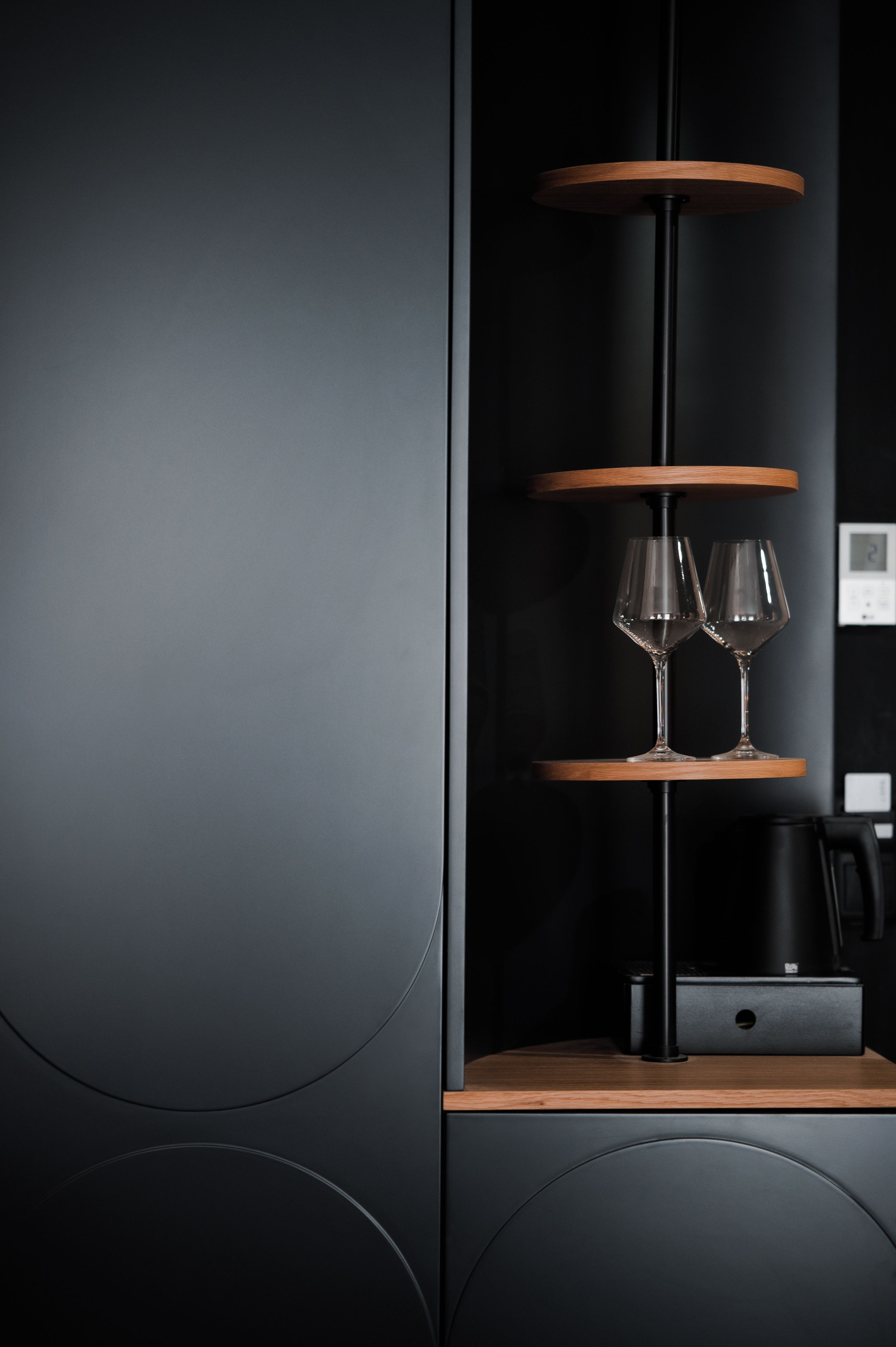 Una pared negra con un estante de madera que sostiene dos copas de vino.