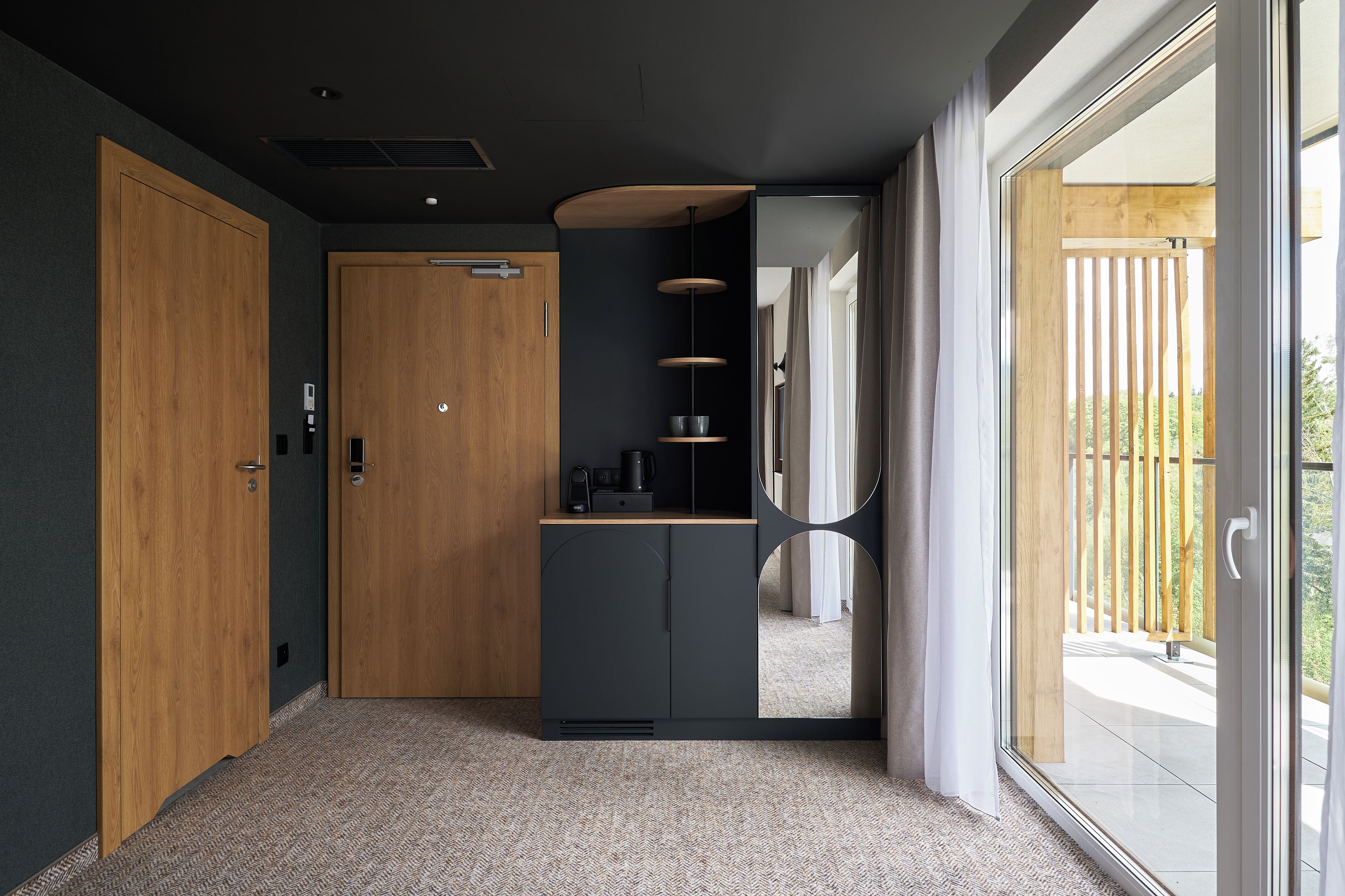 Un interior moderno con una puerta de madera, un armario gris oscuro y una puerta de cristal que da a un área exterior.
