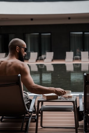A man sitting by a poolside table with a book and a bowl of nuts. - Harmony Valley Resort (Szklarska Poreba)