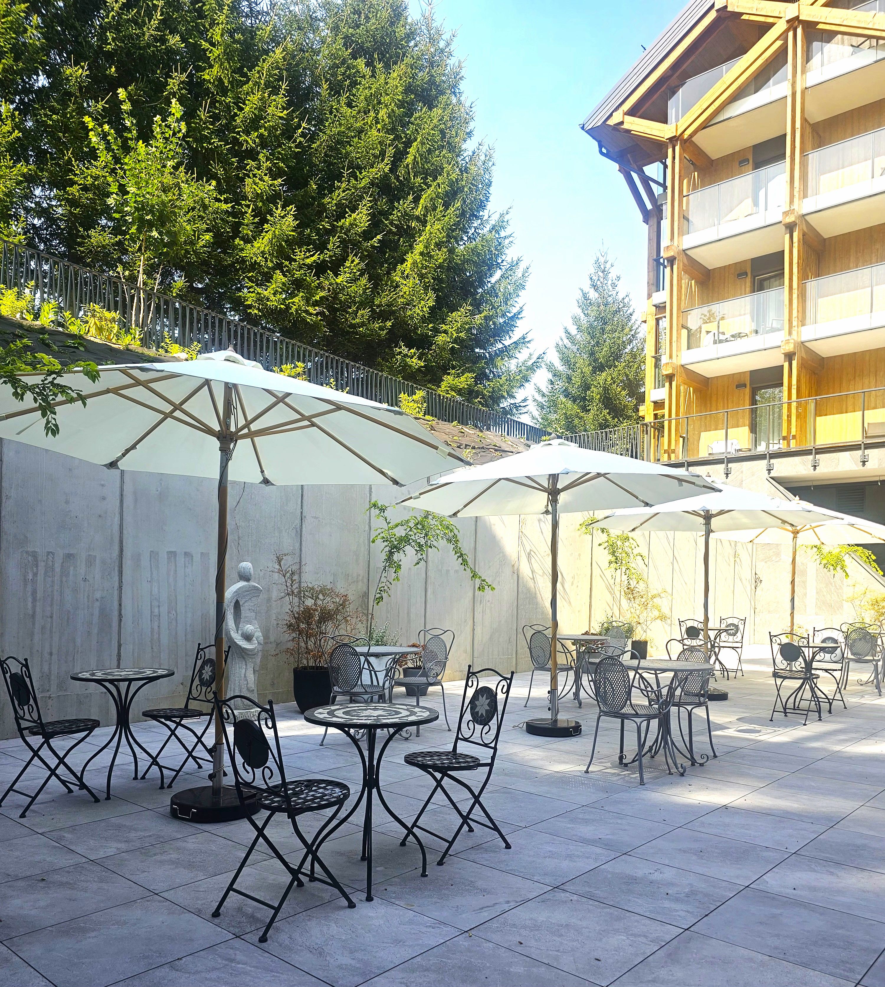 Une terrasse extérieure avec des tables et des chaises, entourée d’une clôture en bois et d’arbres.