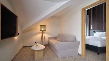 A hotel room with a sofa, a small round table, a floor lamp, a bed, and a TV mounted on the wall.