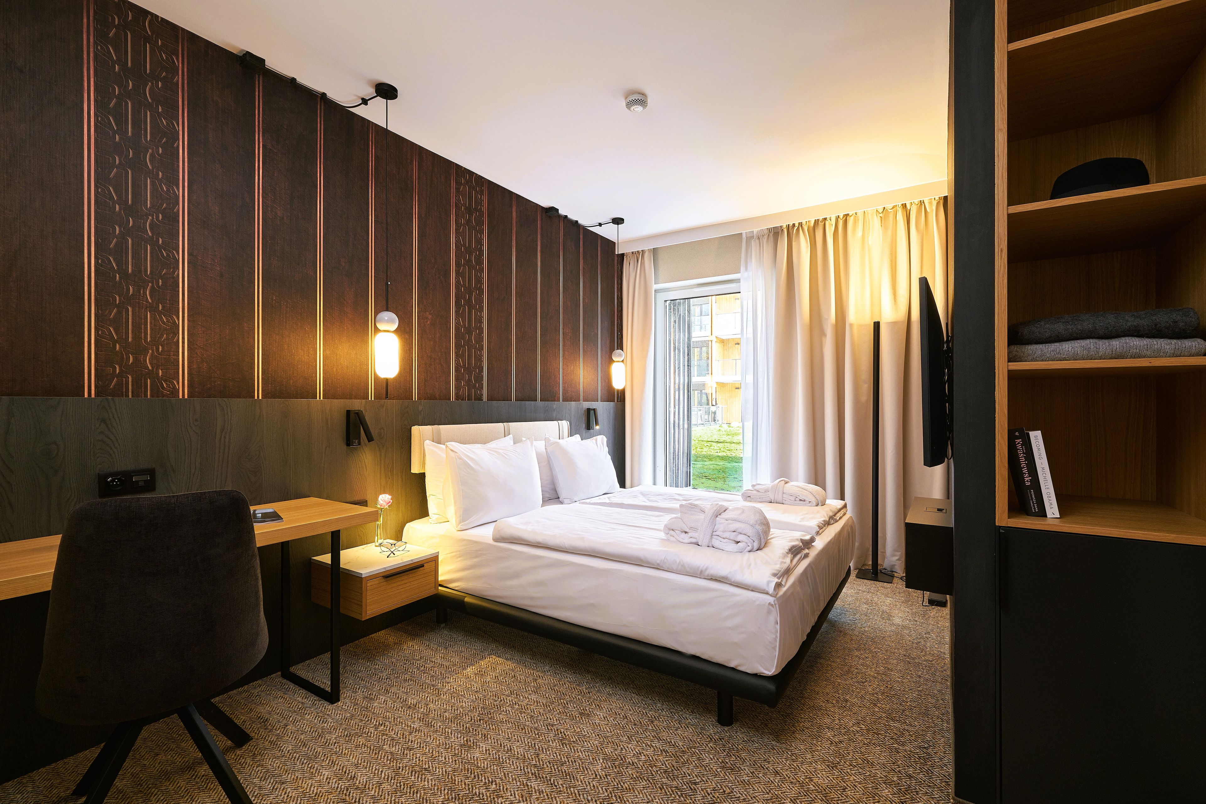 Ein Hotelzimmer mit Bett, Nachttisch, Schreibtisch, Stuhl und Bücherregal.