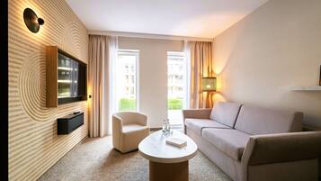 Une chambre d’hôtel équipée d’un téléviseur à écran plat fixé au mur, d’un canapé, d’un fauteuil, d’une table basse et d’une lampe.