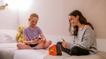 Two individuals sitting on a bed with a game board and cards, a teddy bear, and a wall-mounted light fixture.