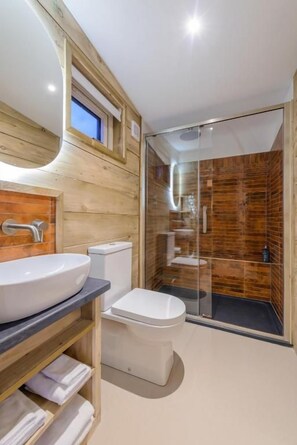 Ein modernes Badezimmer mit einem hölzernen Waschtisch, einem großen Waschbecken, einer Toilette und einer Duschkabine aus Glas.