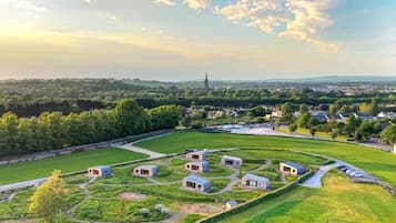 A residential area with multiple houses arranged in a circular pattern, surrounded by green fields and a distant church spire.