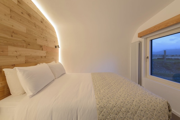 A bedroom with a wooden headboard, a bed with white bedding, a window with a view of the outdoors, and a radiator.