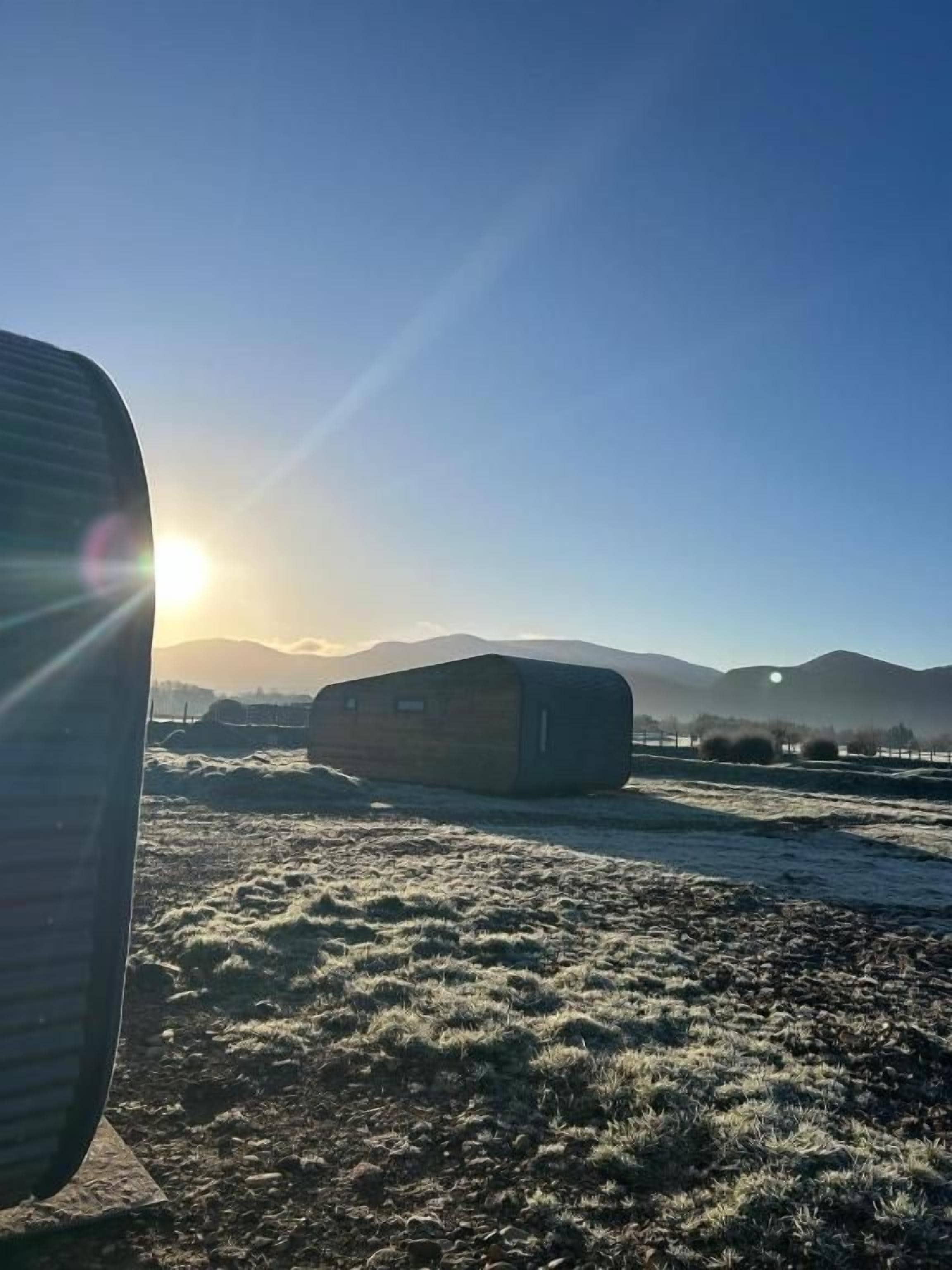 Un edificio con techo inclinado, cielo despejado y sol bajo en el horizonte.