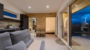 A modern interior with a sofa, a dining area, and a large sliding glass door leading to an outdoor space.