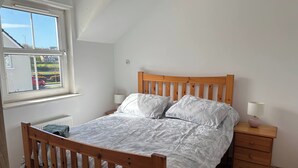 A bedroom with a wooden bed, two bedside tables, a window, and a radiator. - Charming 4-bedroom House in Skibbereen - Pet Friendly Retreat (Skibbereen)