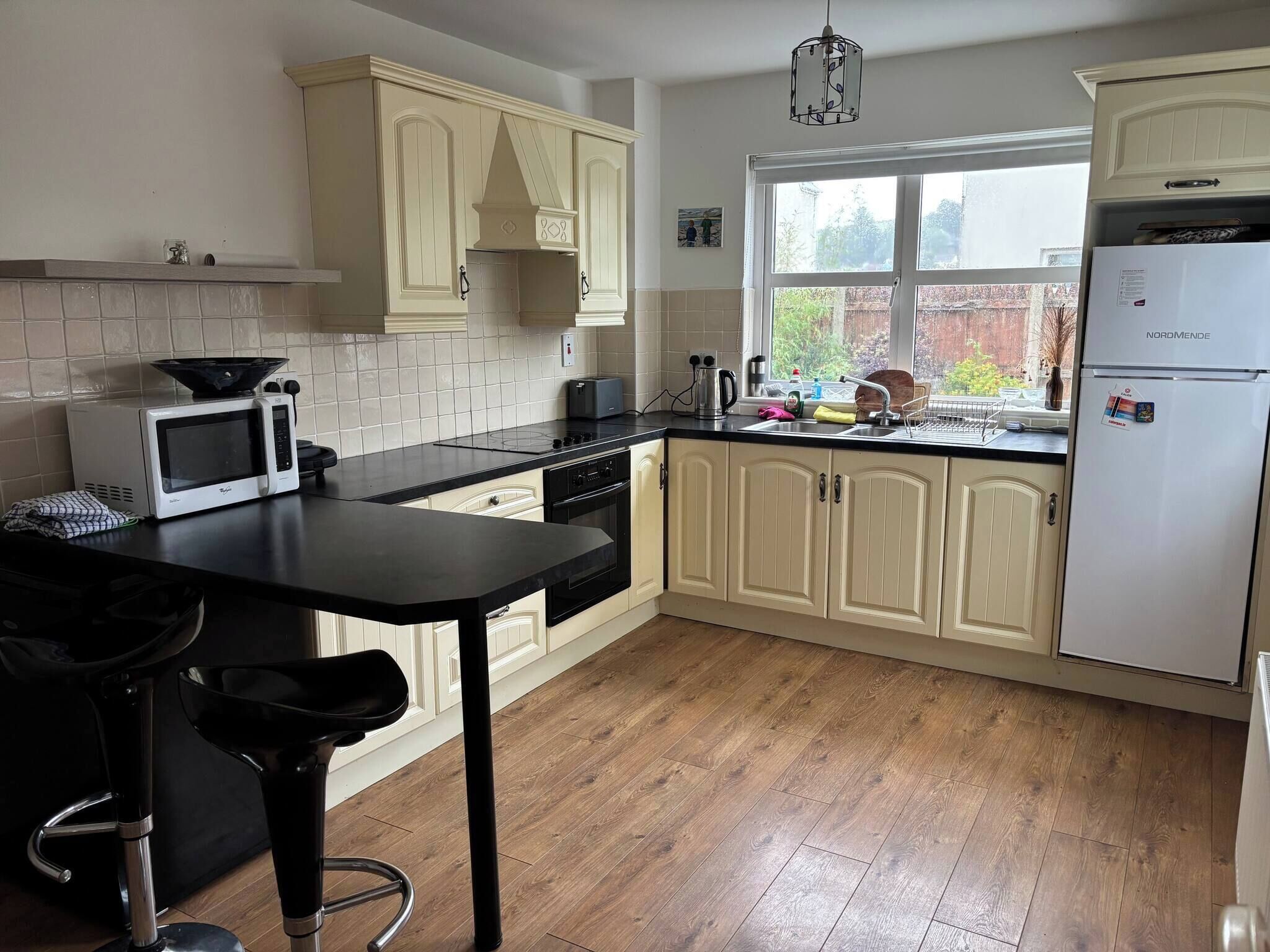 A kitchen with a microwave, toaster, and sink. There are wooden cabinets and a window with a view of the outside.