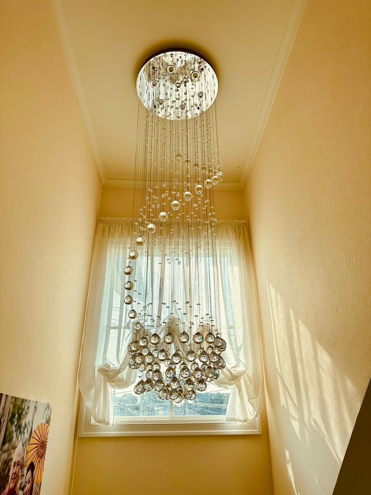 A room with a large window, a hanging chandelier, and a framed picture on the wall.
