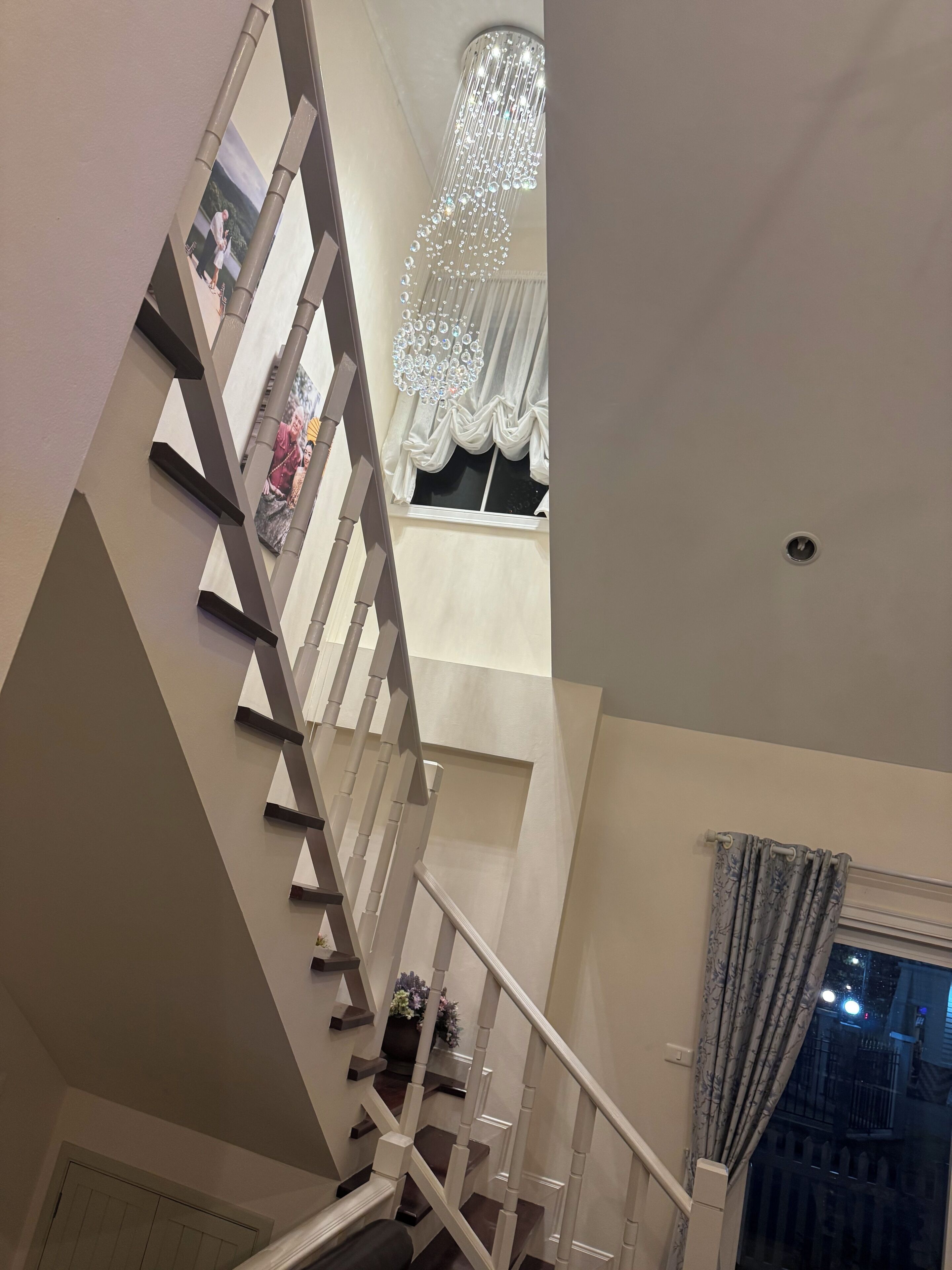 A staircase with a modern design, a chandelier, and a window with curtains.