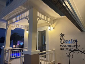 Ein überdachter Außenbereich mit Pool, weißer Brüstung und einem Schild mit der Aufschrift 'Oasis Pool Villa'.