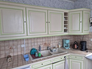 A kitchen with green cabinets, a sink, a kettle, a coffee maker, and a tiled backsplash. - Large village house, 90 m² – Sleeps 10 – Lac du Der – 8 km from Saint-Dizier (Hallignicourt)