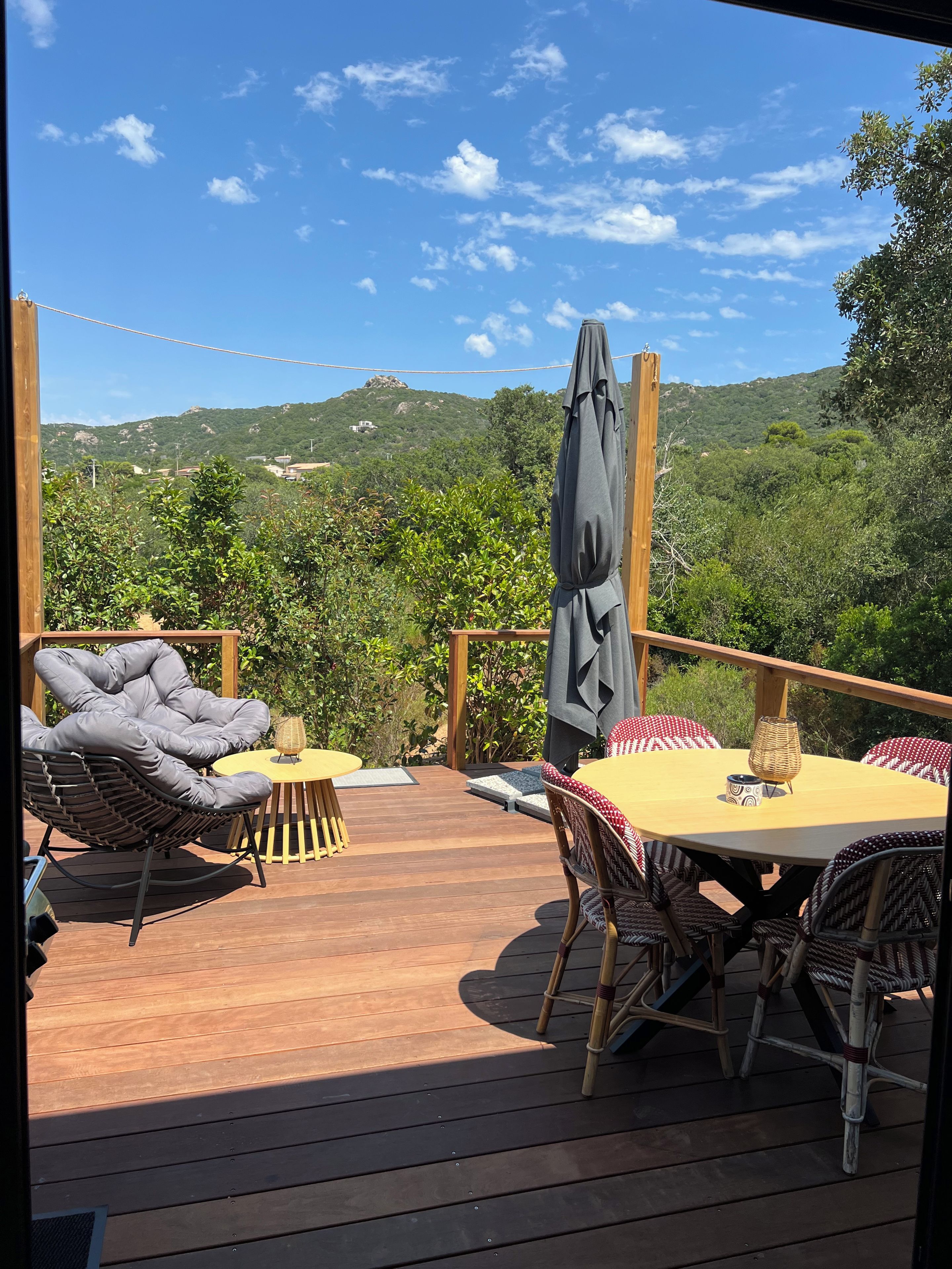 Une terrasse extérieure avec une table ronde et des chaises, entourée de verdure et avec des collines en arrière-plan.