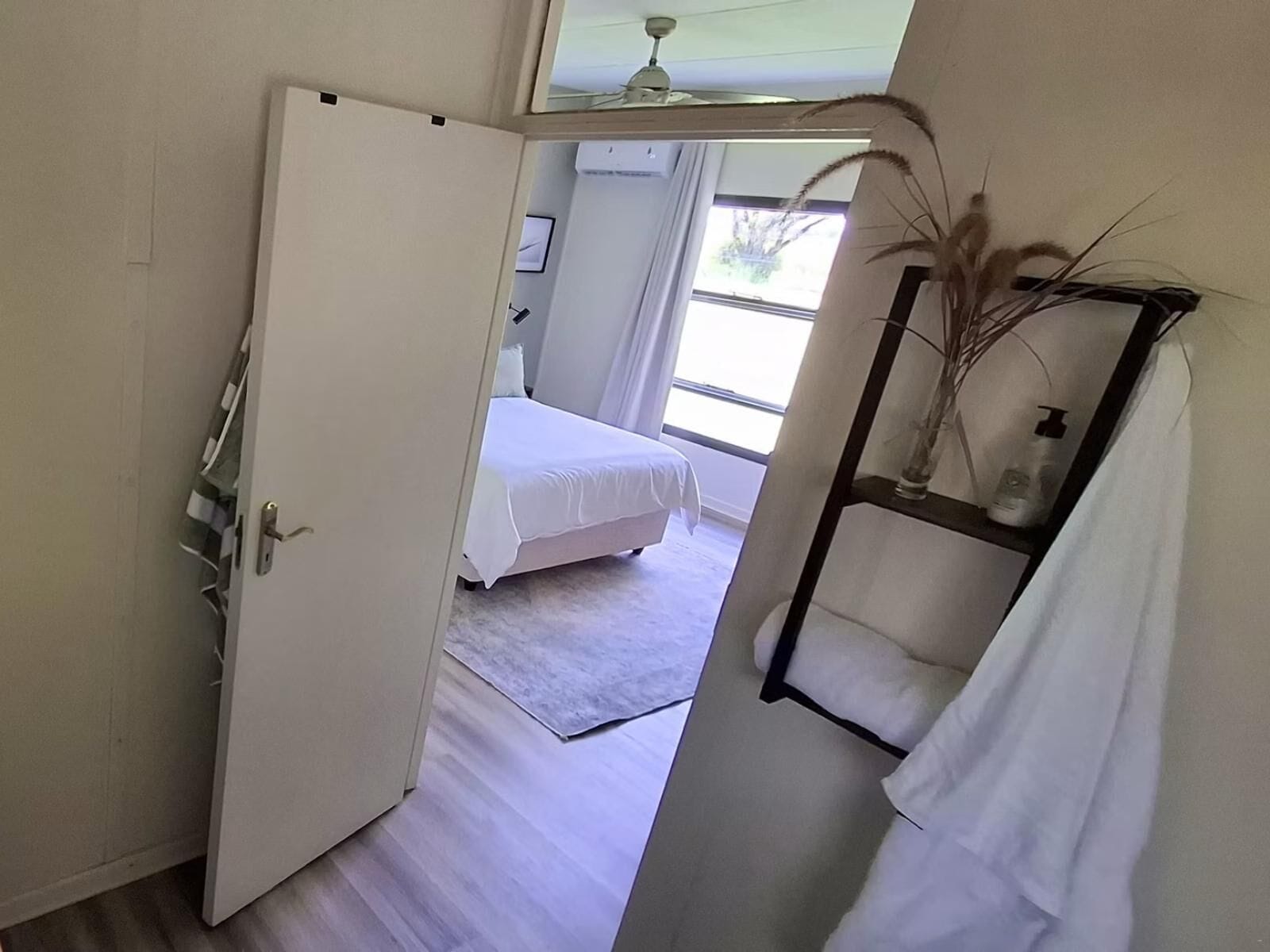 A hotel room with a bed, a bathroom with a towel rack, and a window with natural light.