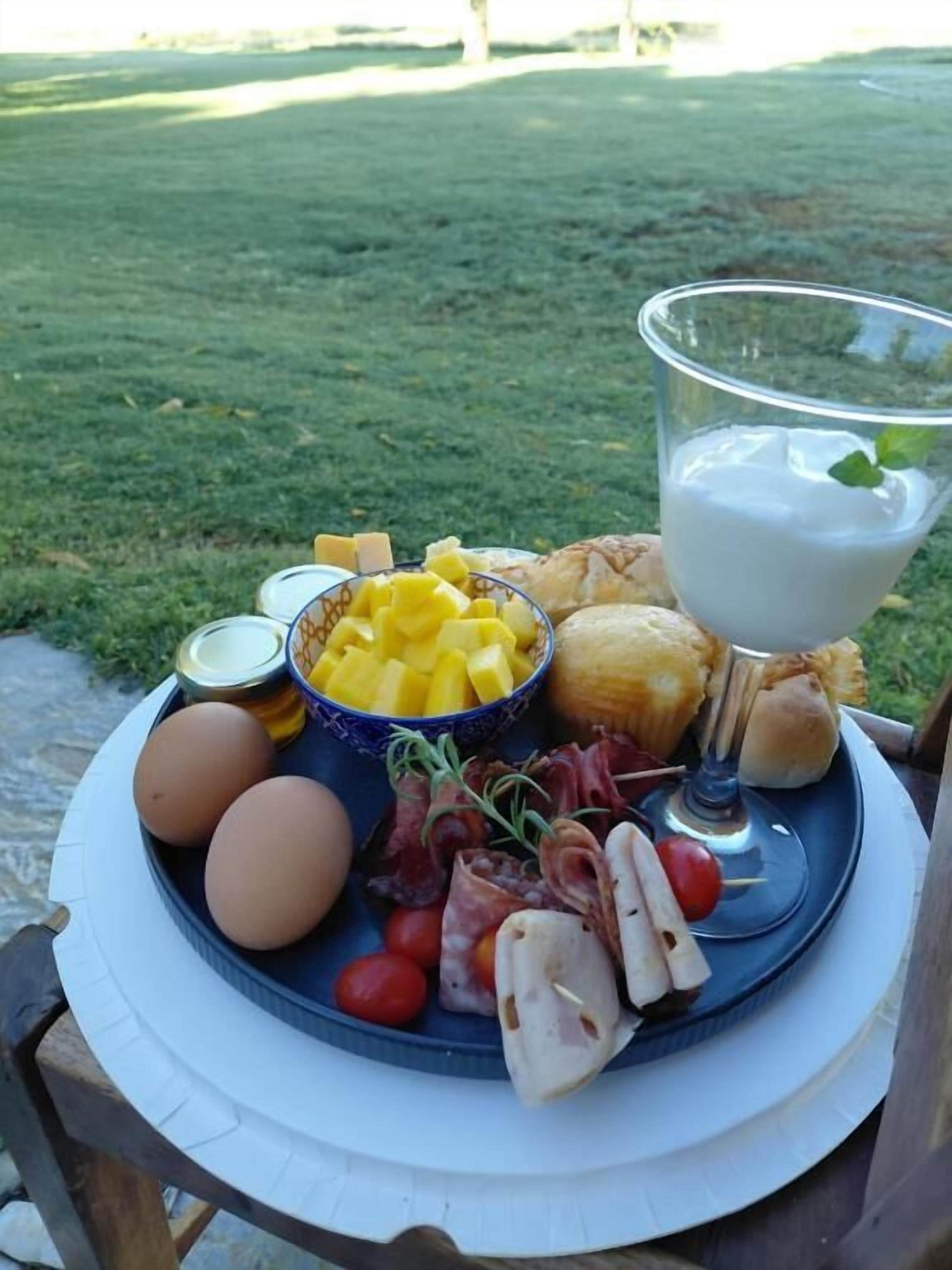 A meal setup on a table with a plate of food, including eggs, cheese, meats, and a bowl of fruit.