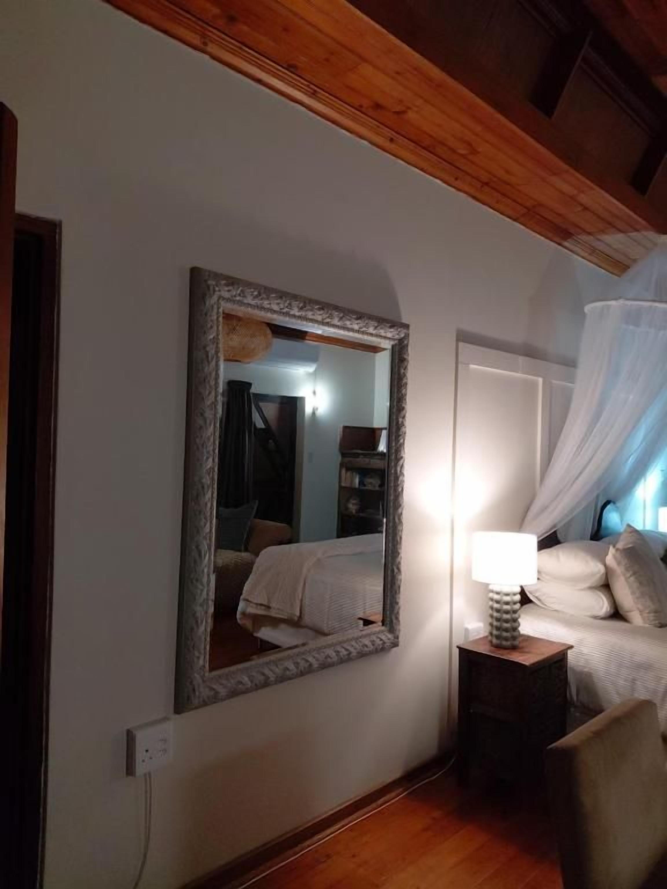 Un dormitorio con un espejo grande, una lámpara de noche, una cama con edredón blanco y una silla.