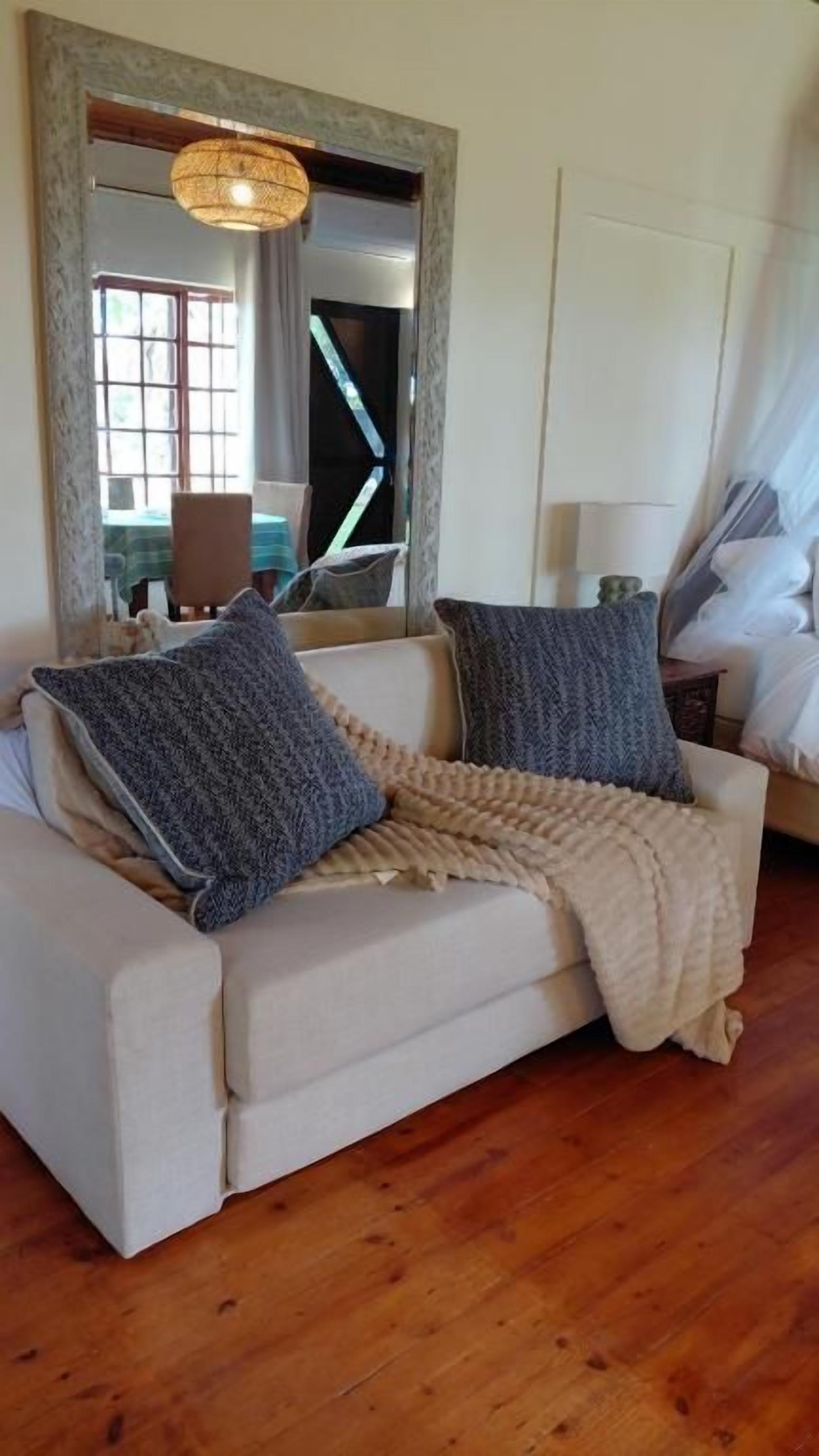 Una sala de estar con un sofá color beige, dos almohadones estampados, un plaid beige, un espejo grande y piso de madera.
