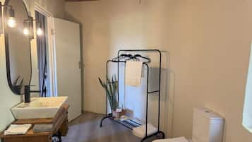 Casa de banho com lavatório branco, sanita, estendal de metal e espelho iluminado.