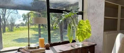 A wooden desk with a lamp, a chair, and a window with a view of greenery.