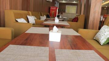 Eine Hotellobby mit Holzwandverkleidung, gelben Sofas mit gemusterten Kissen, einem Holztisch mit Taschentuchbox und einem Coca-Cola-Kühlschrank.