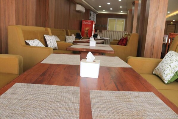 A hotel lobby with wooden panel walls, yellow sofas with patterned cushions, a wooden coffee table with a tissue box, and a Coca-Cola refrigerator. - Junction Hotel (Kathmandu)
