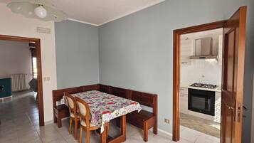 Un coin repas avec une table et des chaises, une cuisine équipée d’une cuisinière et d’un four, et un couloir menant à une autre pièce.