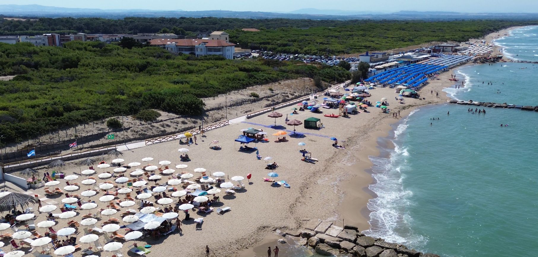 Una platja amb nombrosos para-sols i gandules, un pontó rocos i una vista clara del mar.