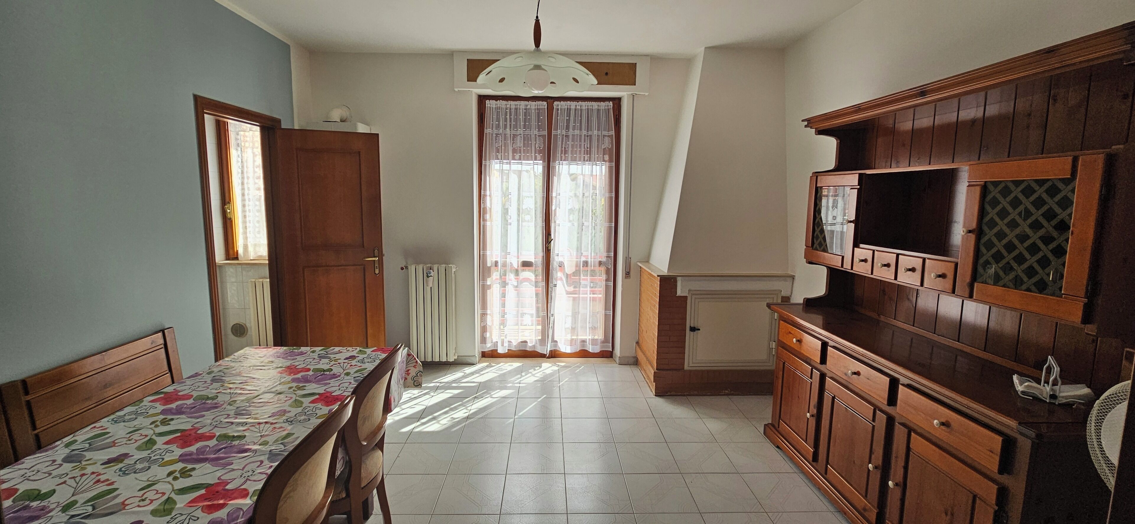 Ein Zimmer mit Esstisch, Holzausbau, Heizkörper und einem fenster mit Vorhängen.