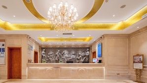 Um saguão com um lustre imponente, uma recepção com escultura em relevo e piso de mármore.