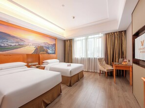 Habitación de hotel con dos camas, un escritorio con una computadora portátil, una silla y un ventanal con cortinas.