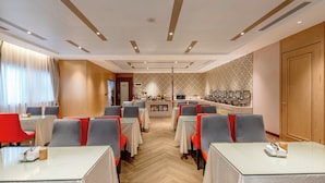 Un comedor de hotel con mesas y sillas, una barra central con una máquina de café y una pared decorada.