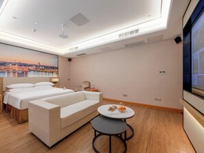 Una habitación de hotel con cama, sofá, una mesita y una pantalla de televisión.